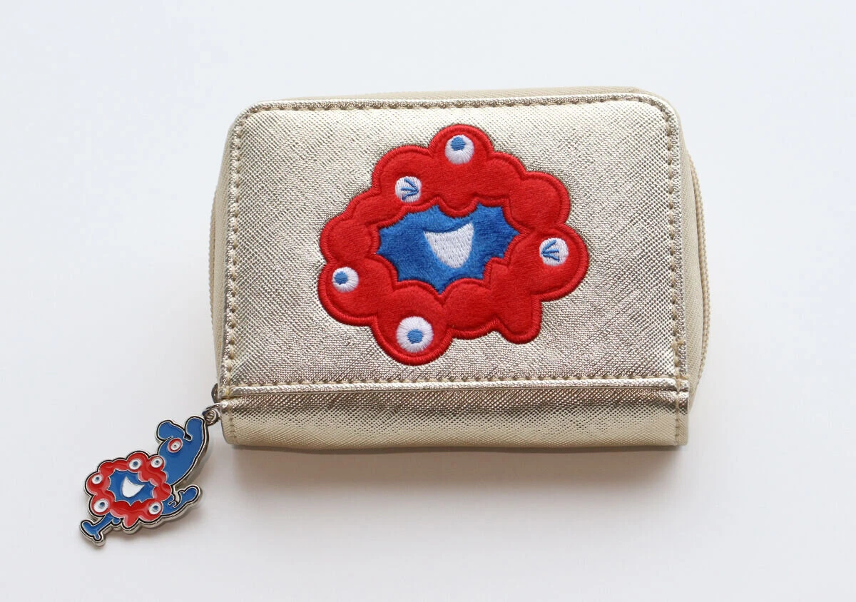 ゴールドのミニ財布の正面アップ。ミャクミャクの赤い刺繍と、ファスナーの引き手についたミャクミャクのチャームが見える ゴールドのミニ財布の正面アップ。ミャクミャクの赤い刺繍と、ファスナーの引き手についたミャクミャクのチャームが見える