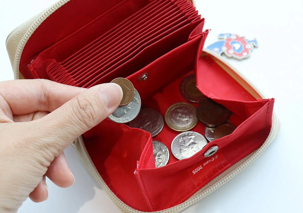 ミニ財布のボックス型小銭入れに硬貨が複数入っており、指で硬貨をつまんでいる様子 ミニ財布のボックス型小銭入れに硬貨が複数入っており、指で硬貨をつまんでいる様子
