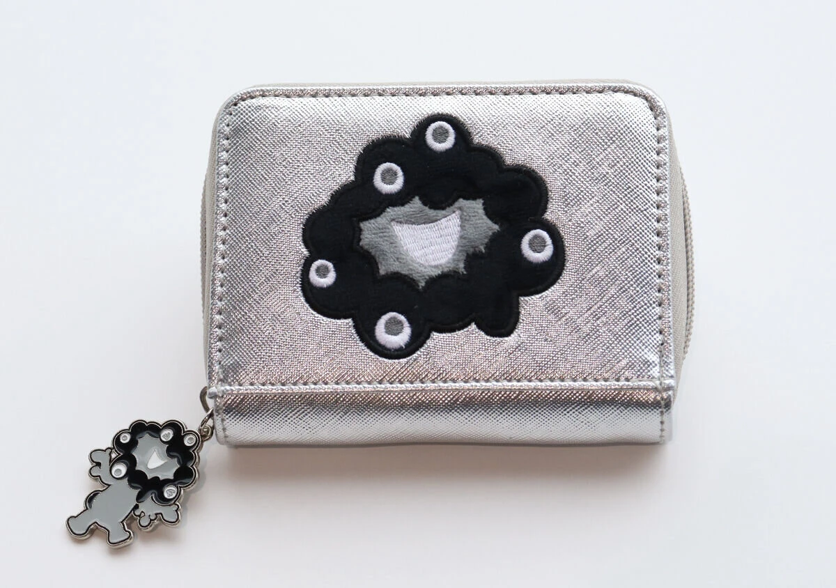 シルバーのミニ財布の正面アップ。黒いミャクミャクの刺繍と、ファスナーの引き手についたミャクミャクのチャームが見える シルバーのミニ財布の正面アップ。黒いミャクミャクの刺繍と、ファスナーの引き手についたミャクミャクのチャームが見える
