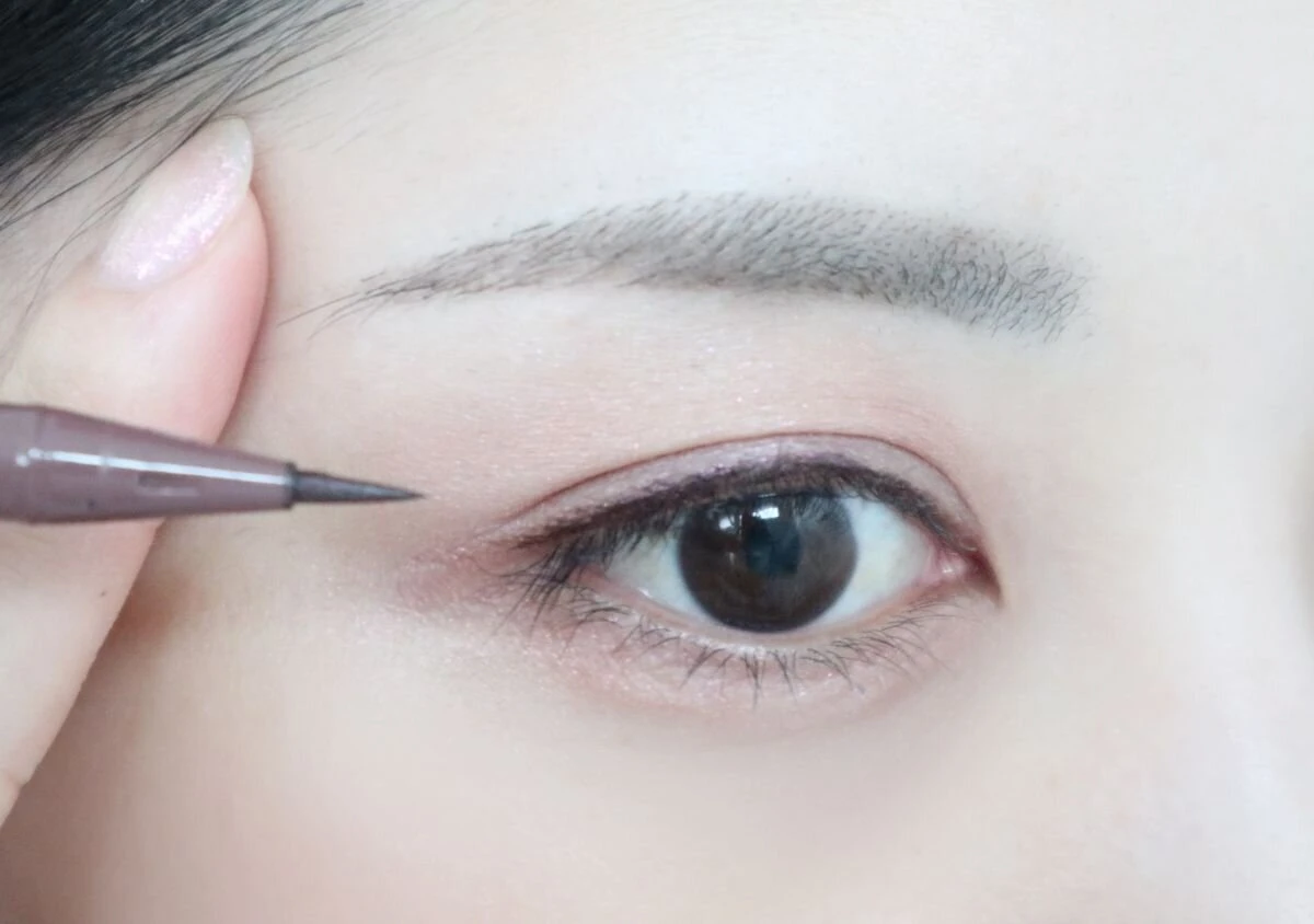 鏡を下に置き目線を下げてアイラインを引く女性 鏡を下に置き目線を下げてアイラインを引く女性
