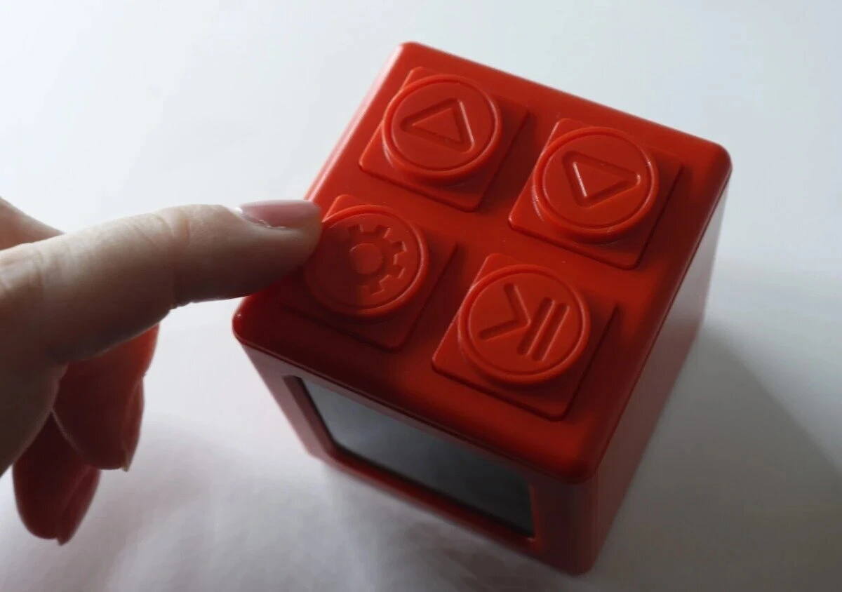 赤いブロック型デジタルタイマー時計の操作ボタンを指で押している様子