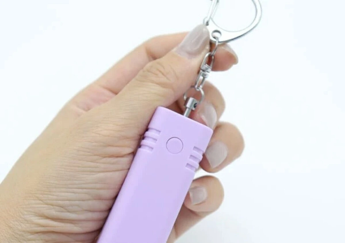 女性の手がラベンダー色の防犯ブザーのチェーンを引っ張っている様子