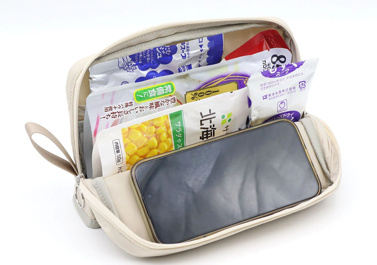 ベージュのポーチのメインスペースにレトルト食品などと一緒にスマートフォンが立てかけられている ベージュのポーチのメインスペースにレトルト食品などと一緒にスマートフォンが立てかけられている