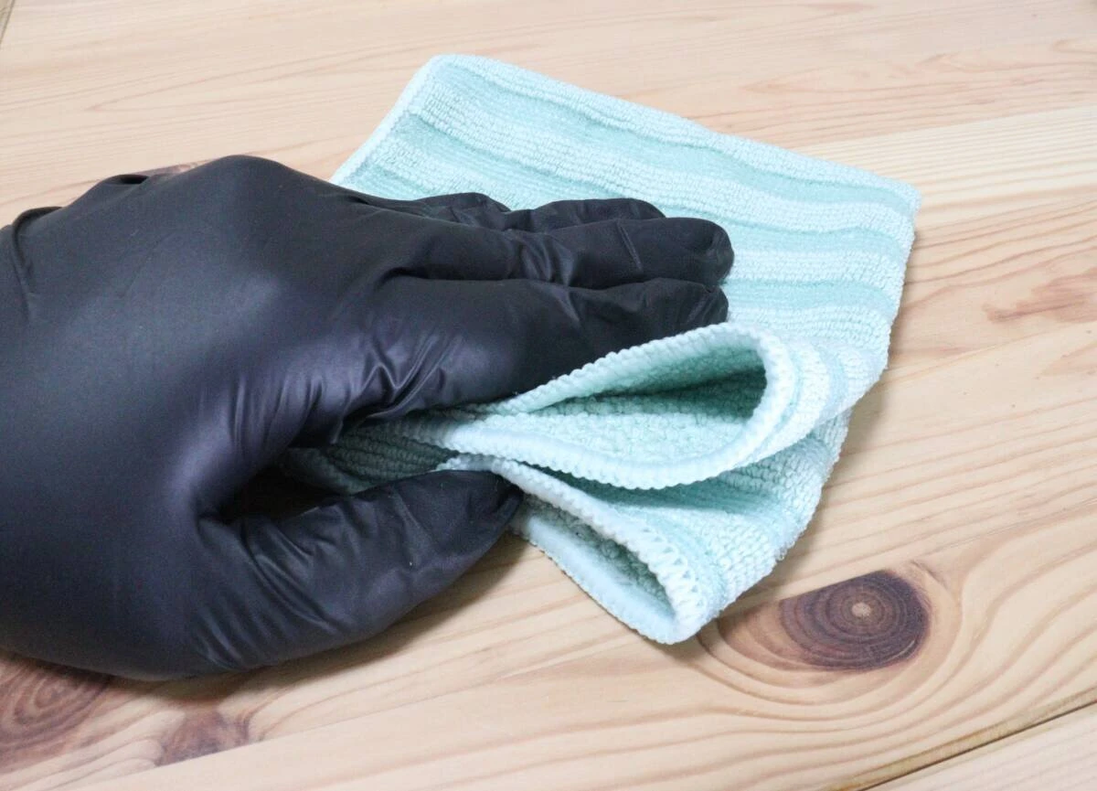 黒い手袋をつけた手で緑色のクロスを持ち木製の棚を拭いている様子