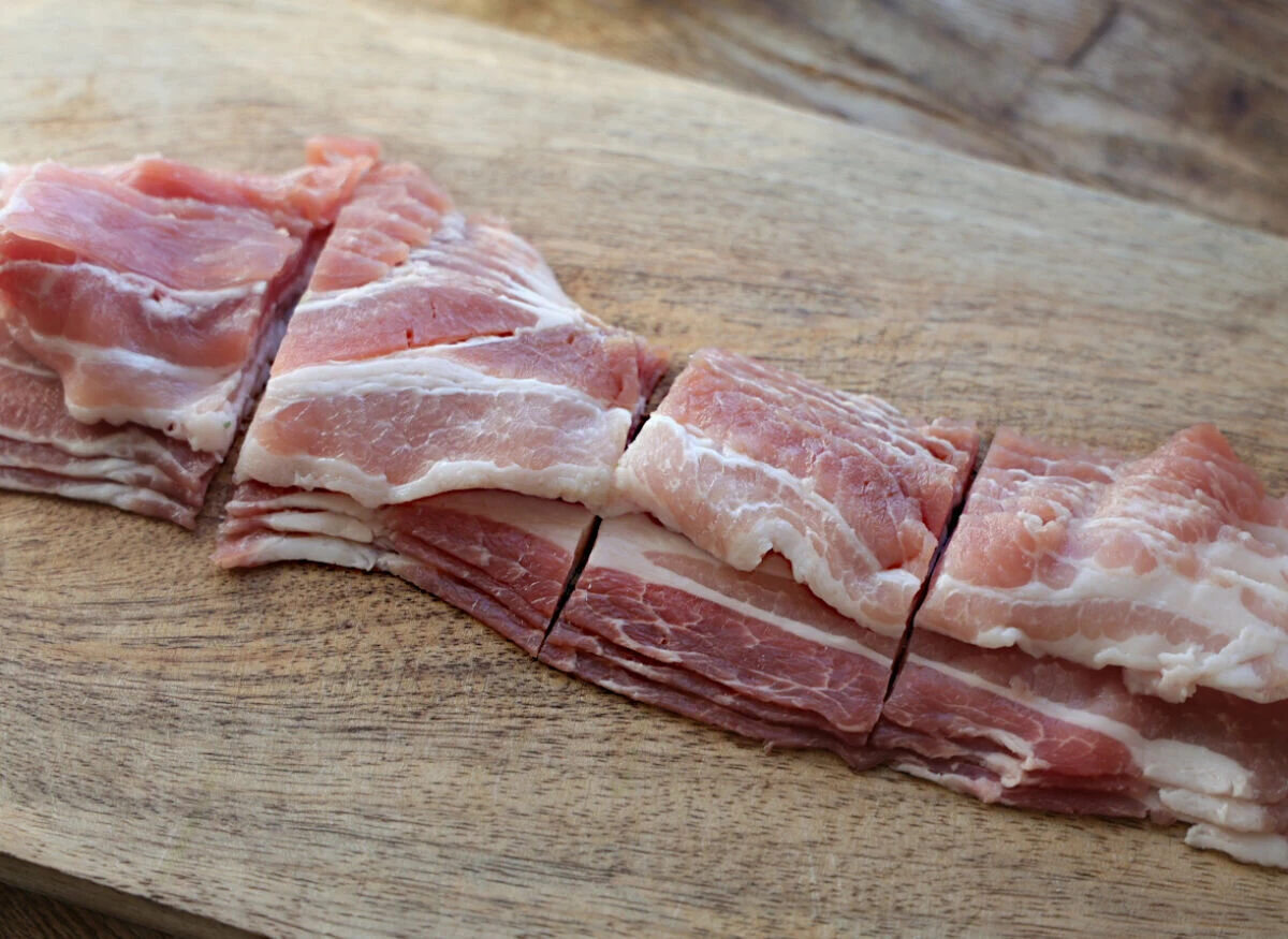 木製のまな板の上で薄切り豚バラ肉を包丁で切っている様子