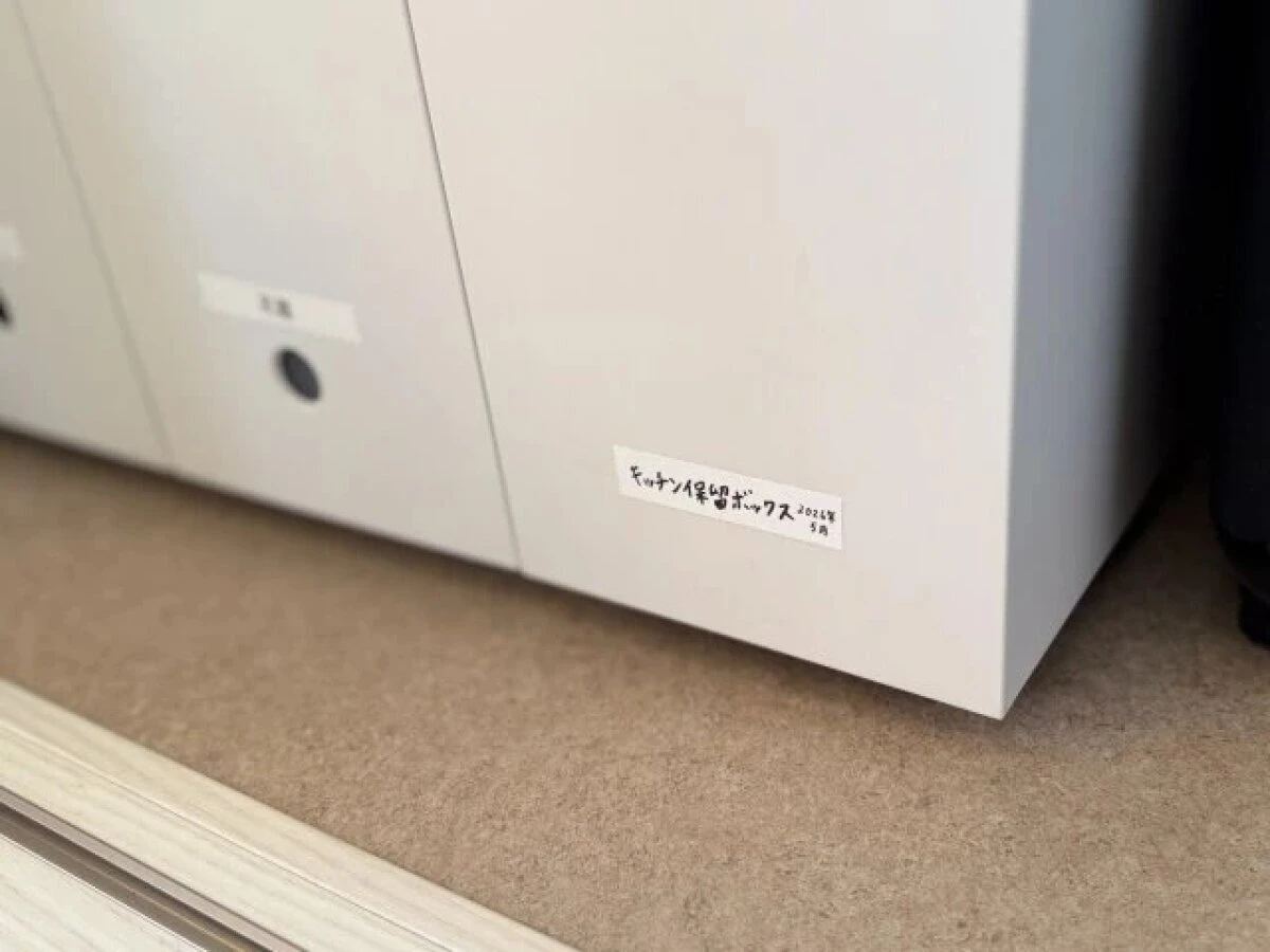白い収納棚の扉に「キッチン保管ボックス 202X年 5月」と手書きされたラベルが貼られている