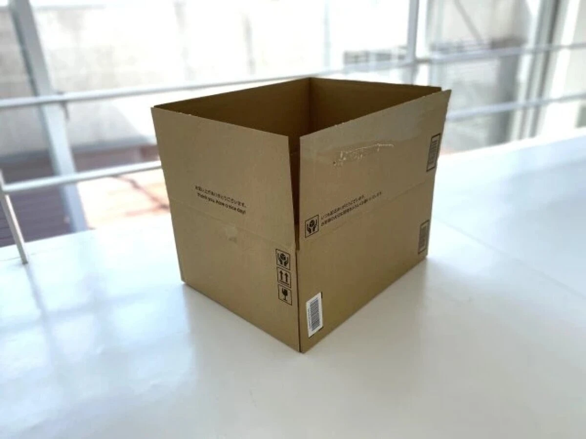 白いテーブルの上に、開いた状態の茶色い段ボール箱が置かれている