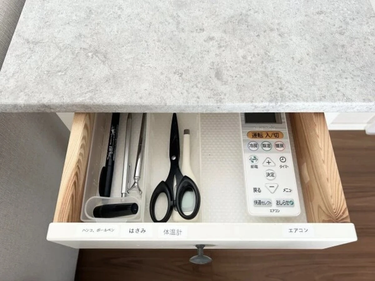 引き出しの中に、ペンやハサミ、体温計、エアコンのリモコンが仕切りを使って整理されている