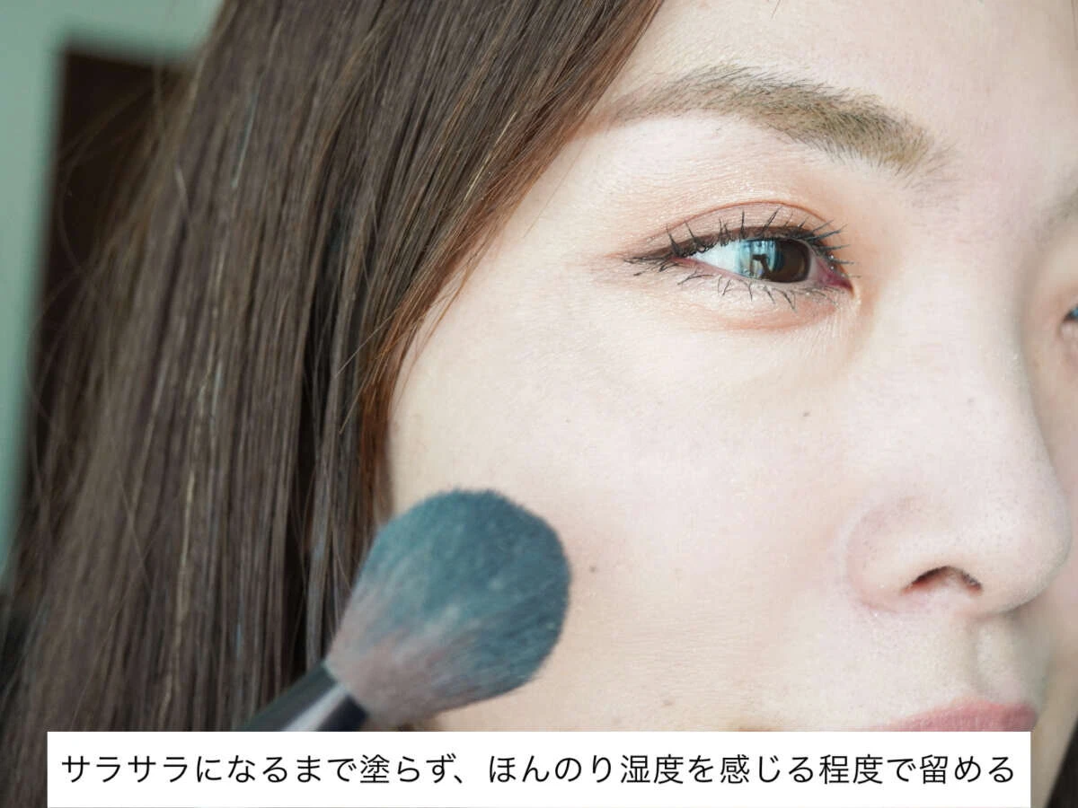 40代女性が頬にフェイスパウダーをブラシで軽く塗布している。