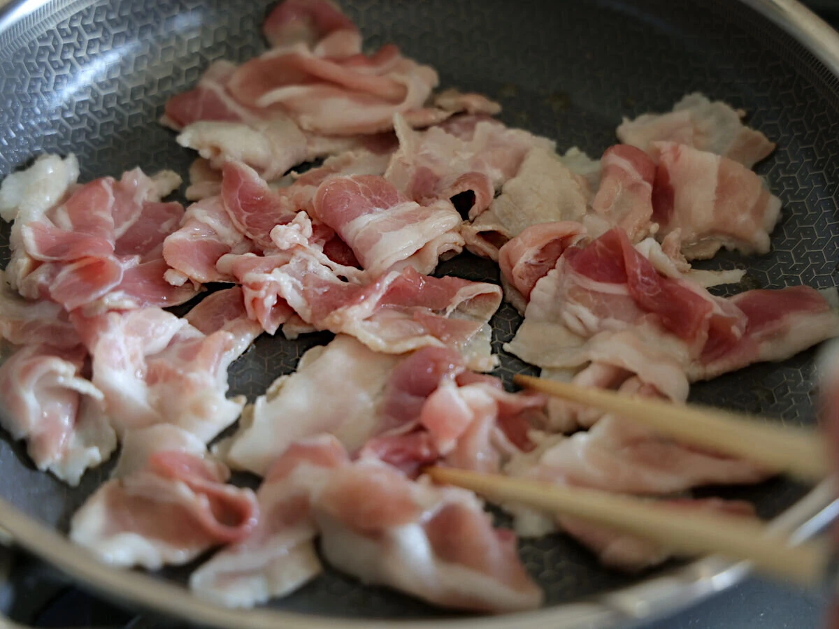 フライパンにひいたごま油で薄切り豚バラ肉を炒めているところ