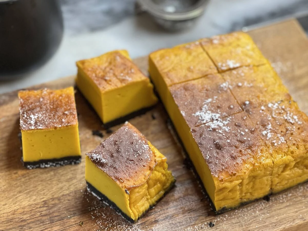 木製のカッティングボードに切り分けられたしっとりかぼちゃケーキと粉糖