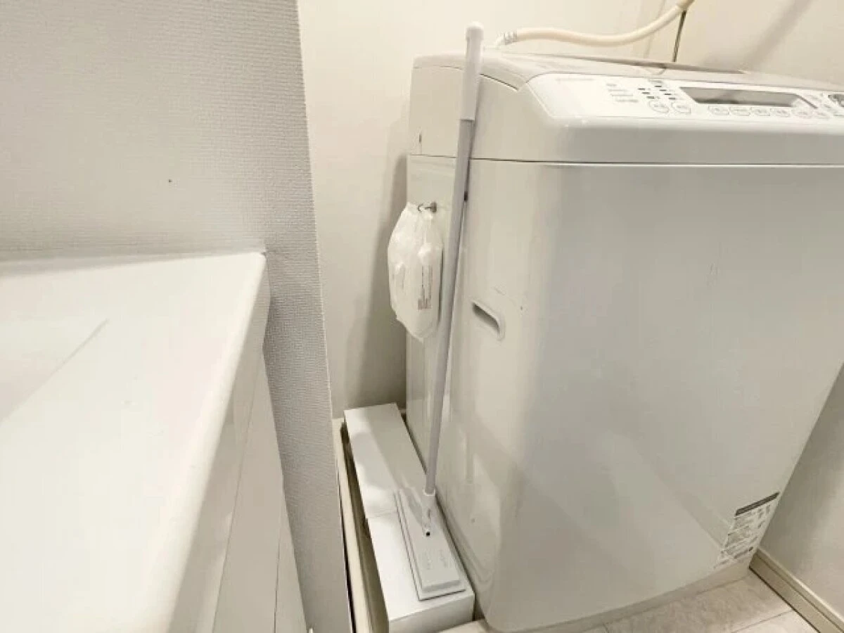 洗濯機横の狭い隙間にフローリングワイパーと掃除道具を置いている様子 洗濯機横の狭い隙間にフローリングワイパーと掃除道具を置いている様子