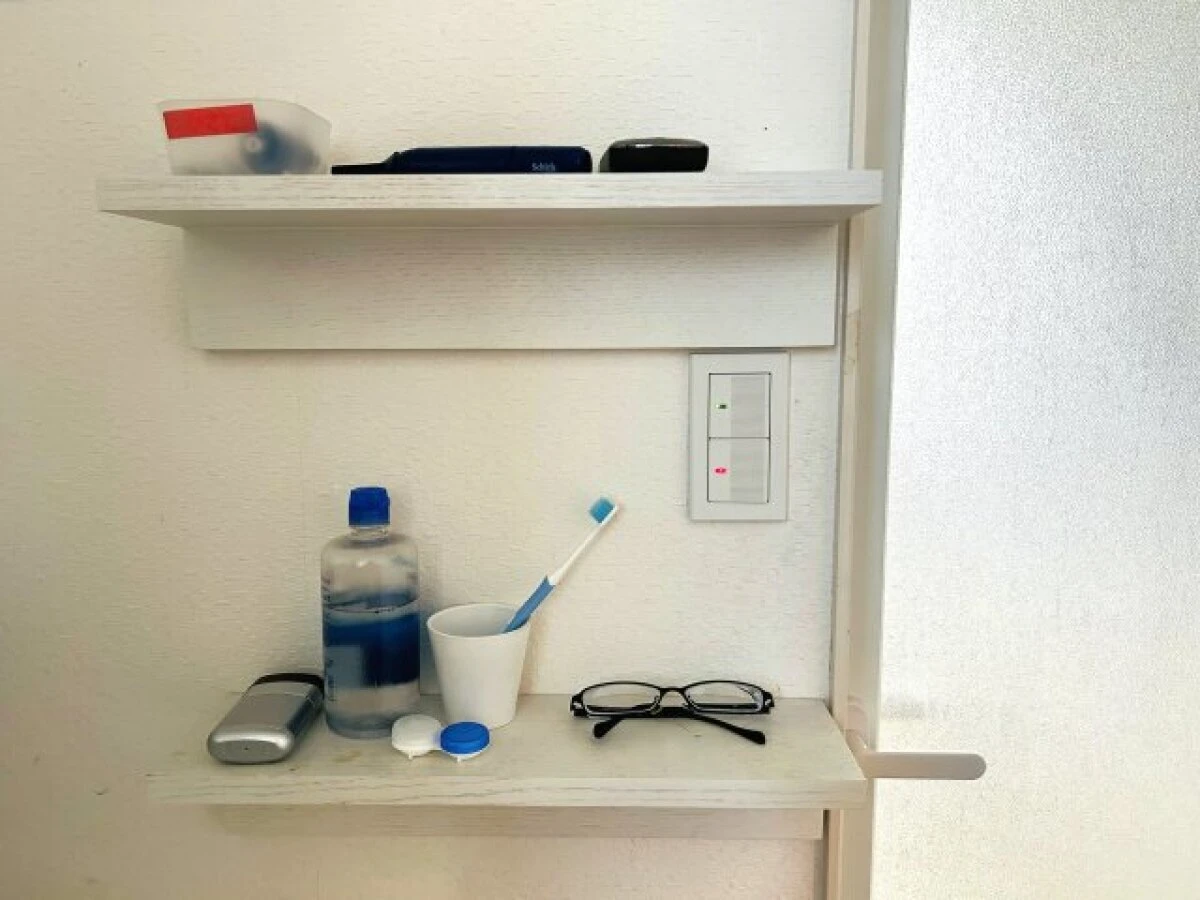 壁に付けられる家具棚の上に歯ブラシやコンタクト用品などの小物を並べて置いている様子