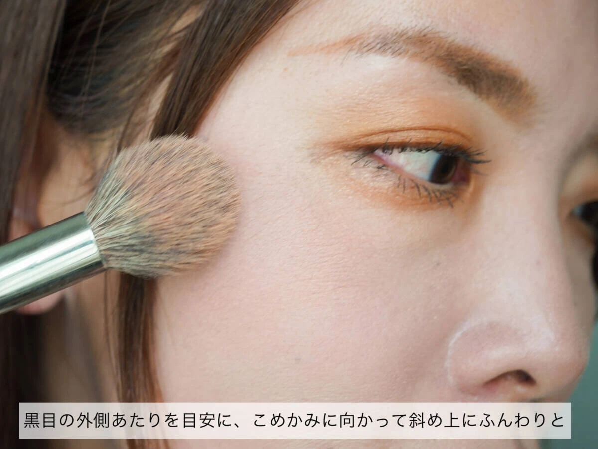 チークブラシを使い黒目の外側からこめかみに向かってぼかしている女性の横顔 チークブラシを使い黒目の外側からこめかみに向かってぼかしている女性の横顔