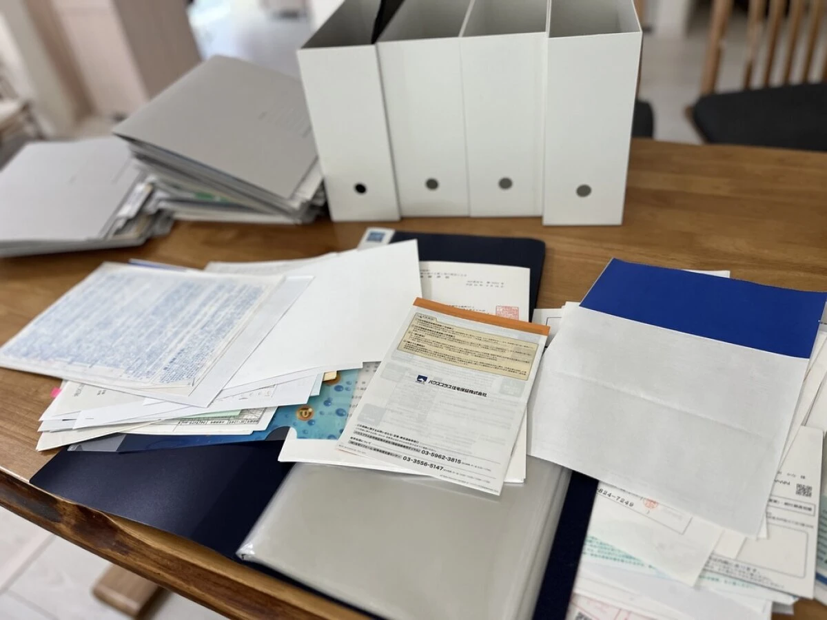 木目のテーブルの上に散らばった書類や郵便物と白いファイルボックス
