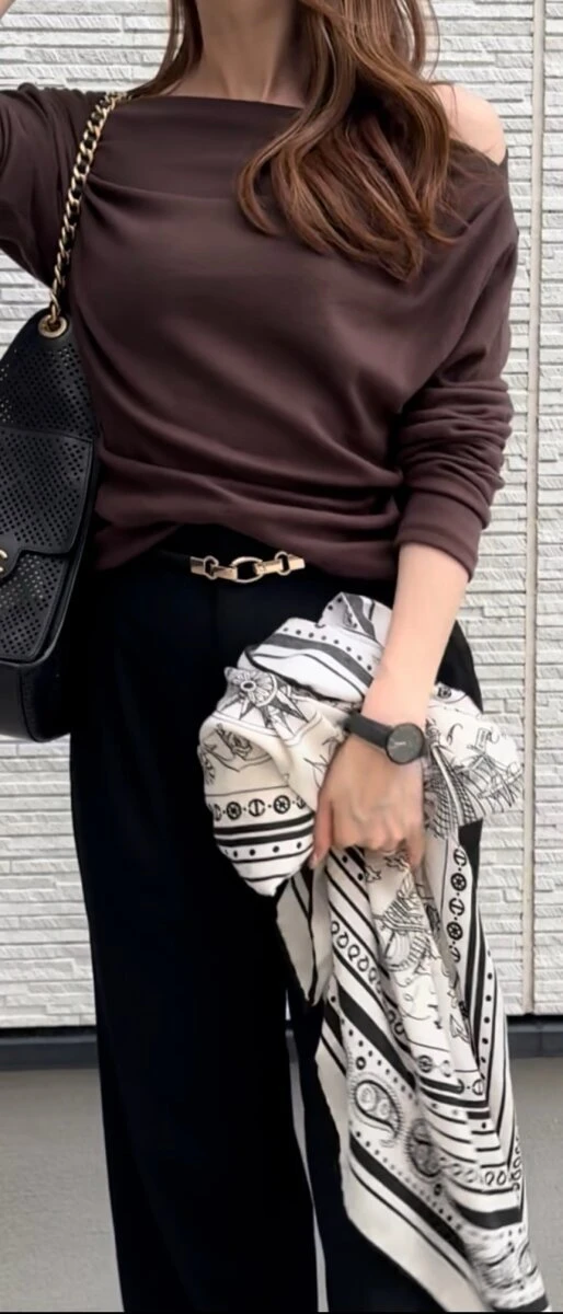 ブラウンのトップスに黒パンツを合わせ白黒のスカーフを手にした女性
