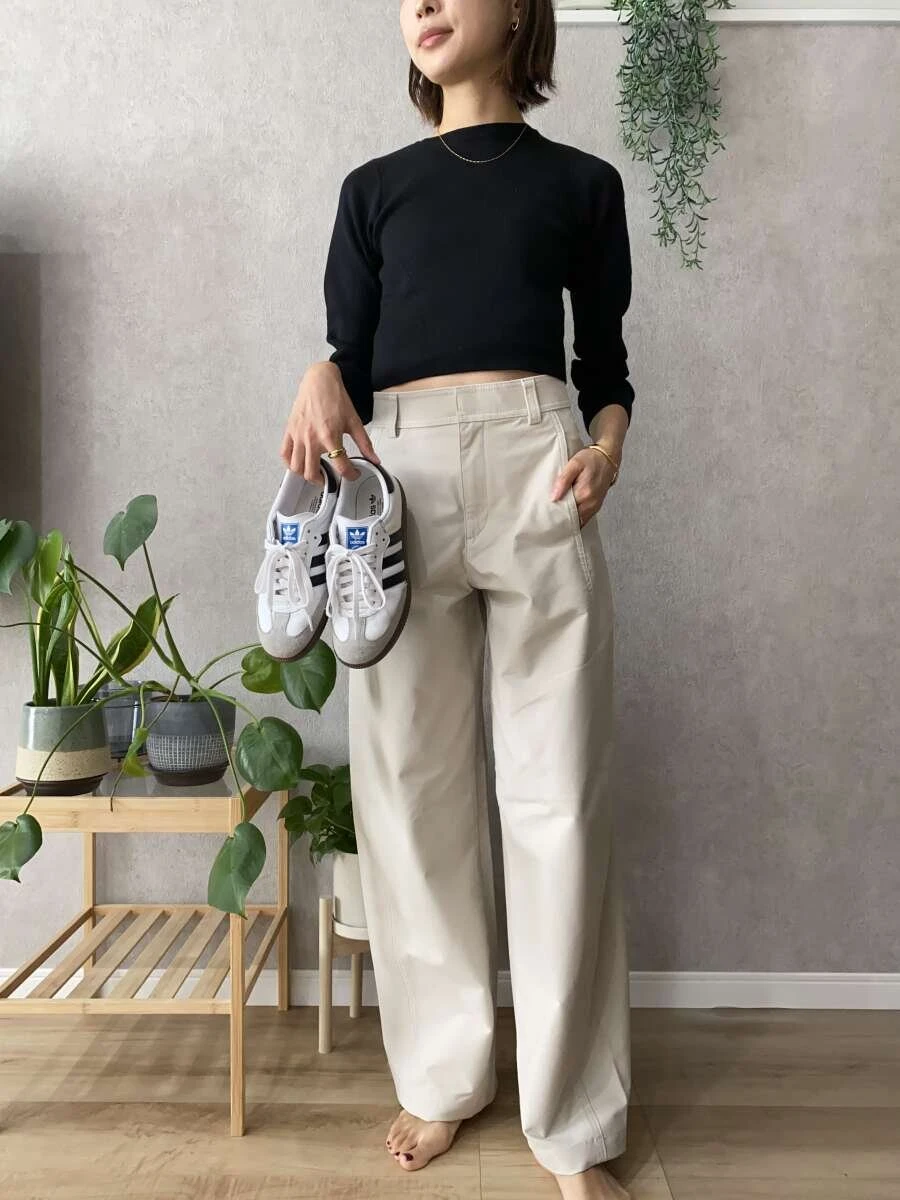 黒のクロップド丈ニットにナチュラルのパンツを合わせ、スニーカーを持っている女性