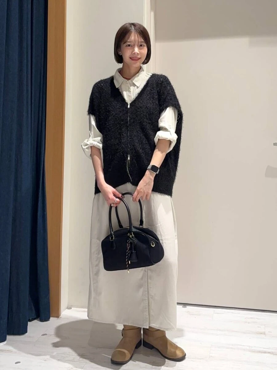 白のシャツワンピースに黒のシャギーベストを重ね黒いバッグを持つショートヘアの女性 白のシャツワンピースに黒のシャギーベストを重ね黒いバッグを持つショートヘアの女性