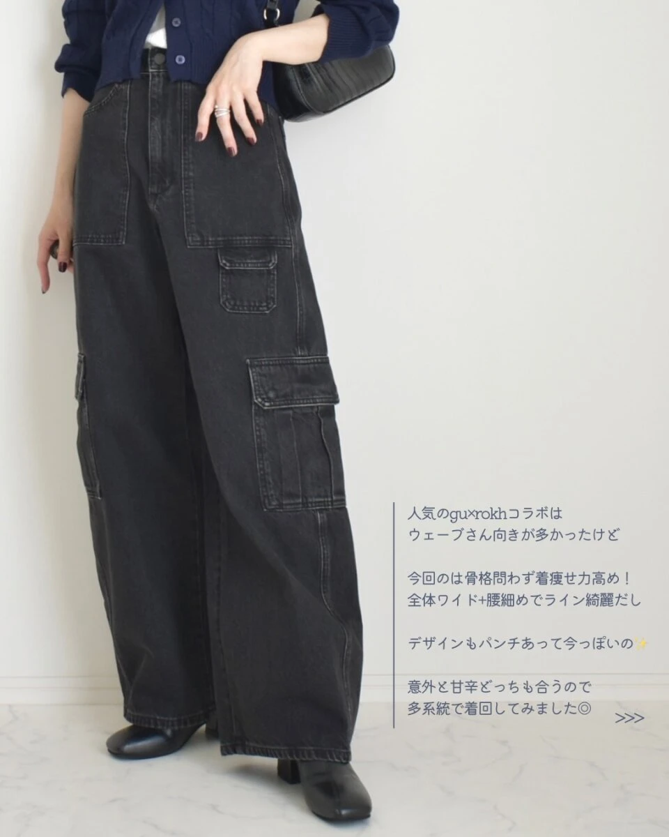 黒いバレルユーティリティジーンズとネイビーのカーディガンを着用し、黒いバッグを持つ女性の全身