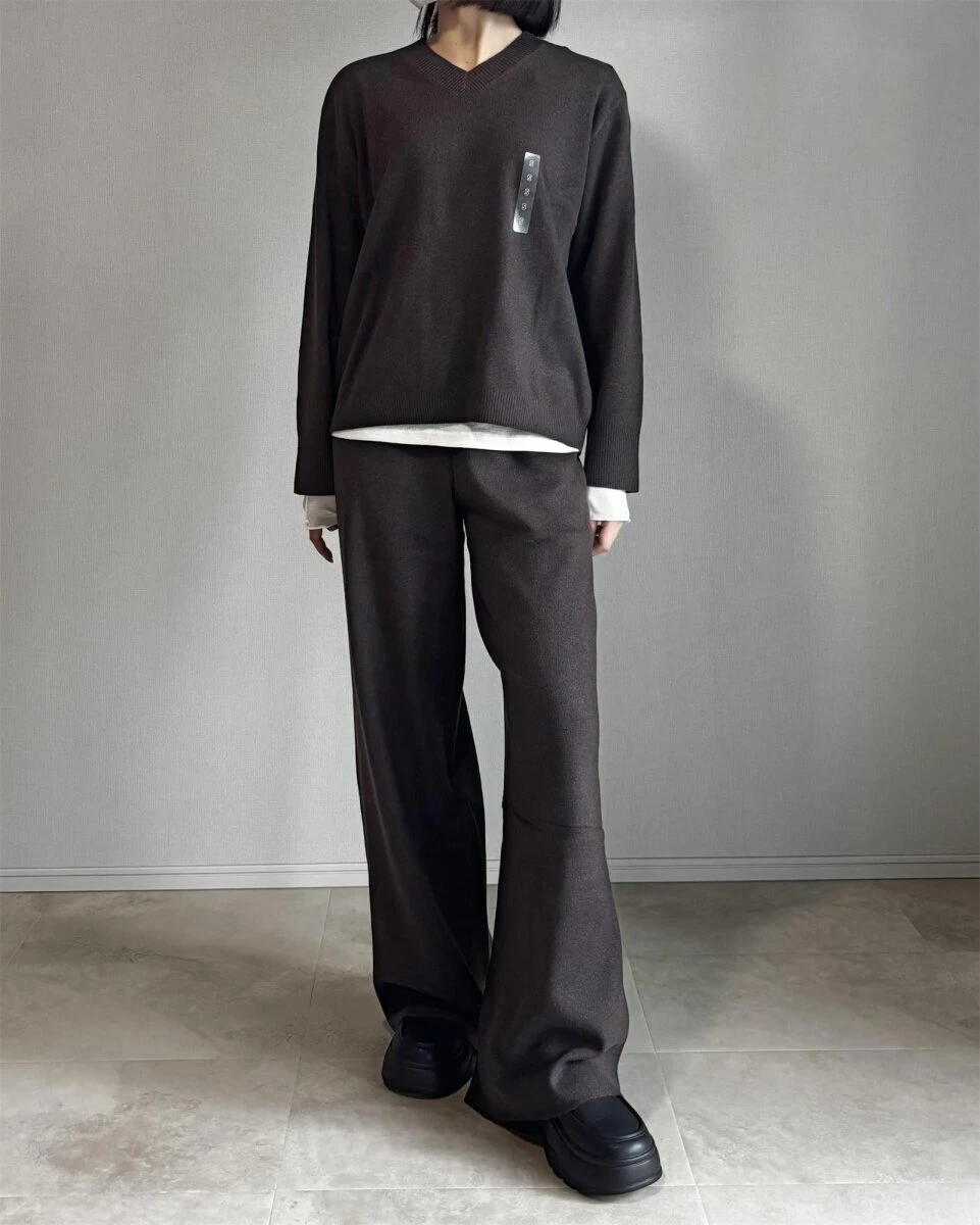 ダークブラウンのニットパンツに同色のVネックニットと白Tシャツを合わせたセットアップ風コーデの女性